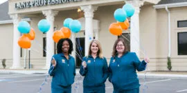 Smiling staff wearing blue scrubs holding teal and orange balloons in Hamlet