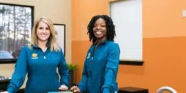 Two orthodontic assistants smiling in front of orange wall